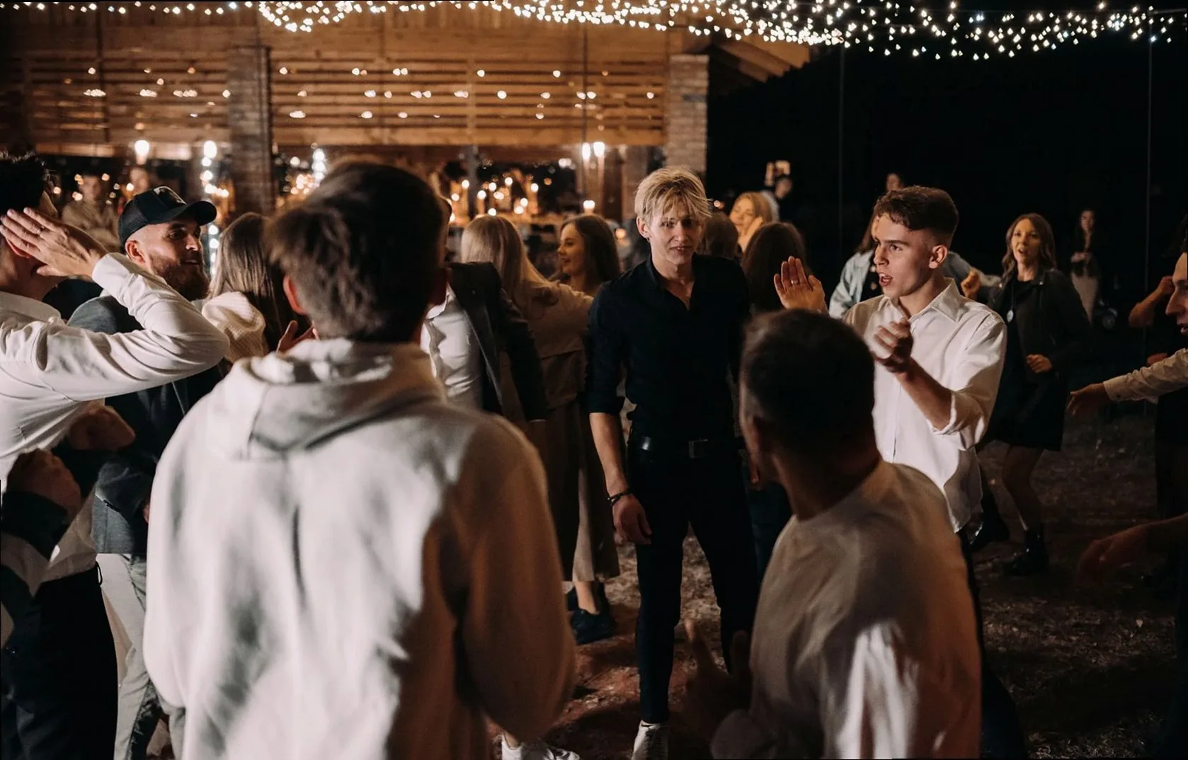 Guests enjoy an energetic night of dancing under string lights at an outdoor wedding.